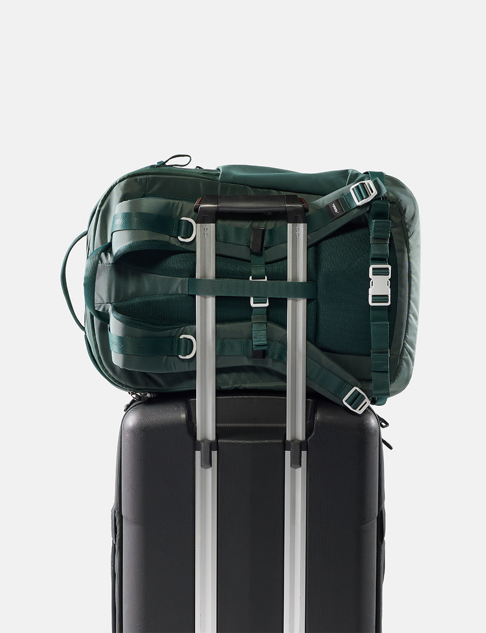 Matador 30L Carry-On Travel Pack in Juniper - green backpack on top of a black suitcase with silver handles on a white background