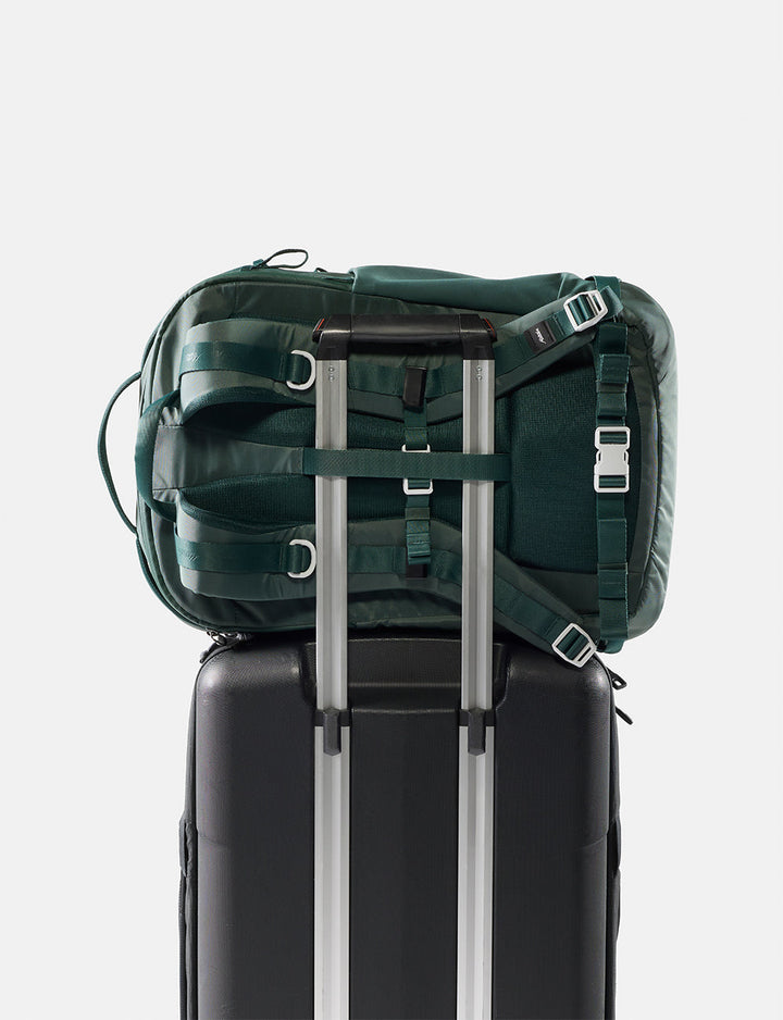 Matador 30L Carry-On Travel Pack in Juniper - green backpack on top of a black suitcase with silver handles on a white background