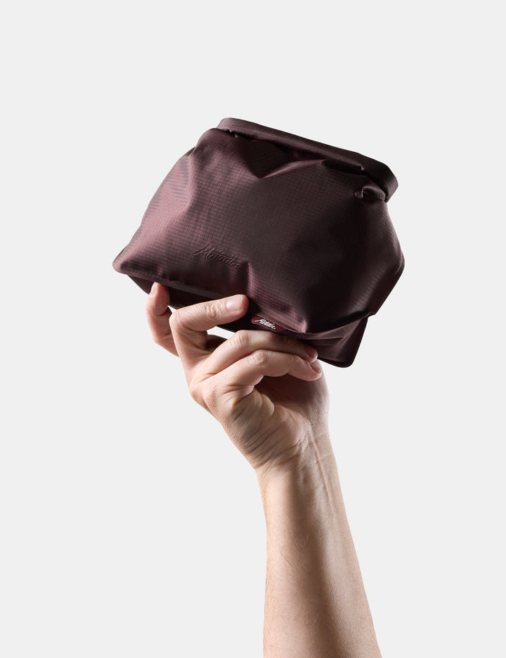 Matador FlatPak Waterproof Toiletry Case (V2) in Garnet - hand holding a Garnet toiletry bag against a white background