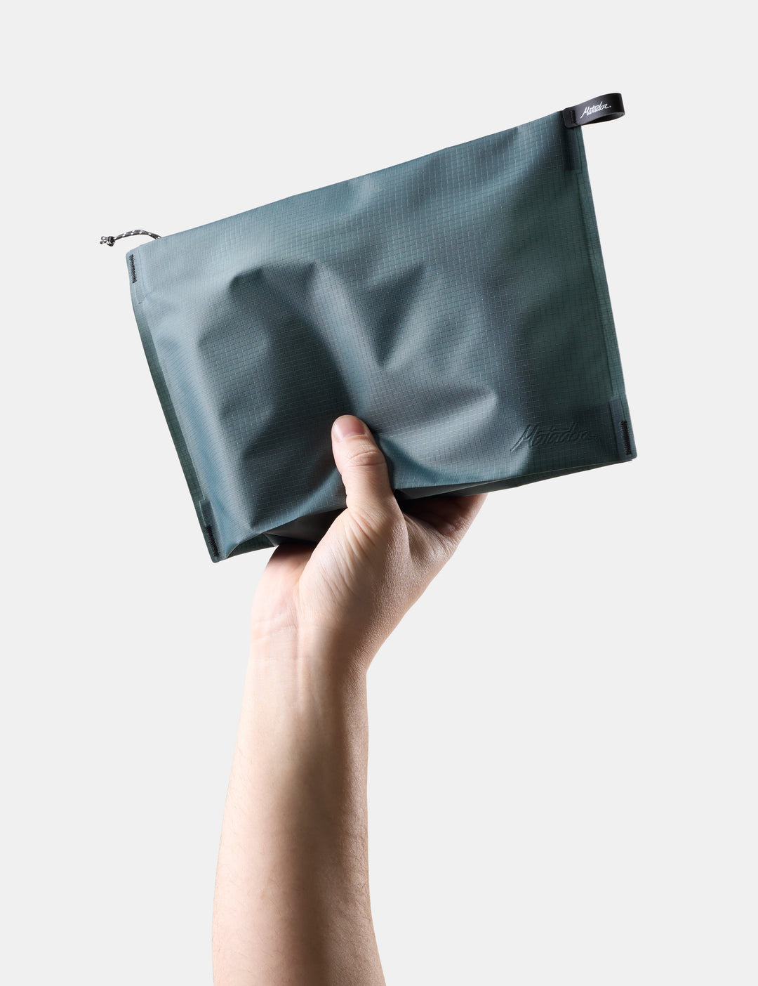 Matador FlatPak Zipper Toiletry Case (V2) in Juniper - hand holding a Blue-green zipper toiletry case against a light background
