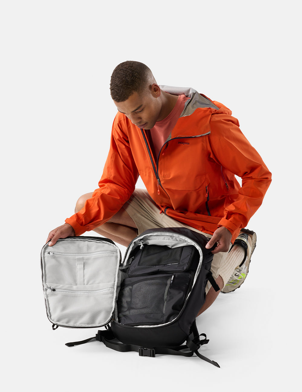 Matador 24L Adventure Pack in Black - person in an orange jacket opening a black backpack on a white background