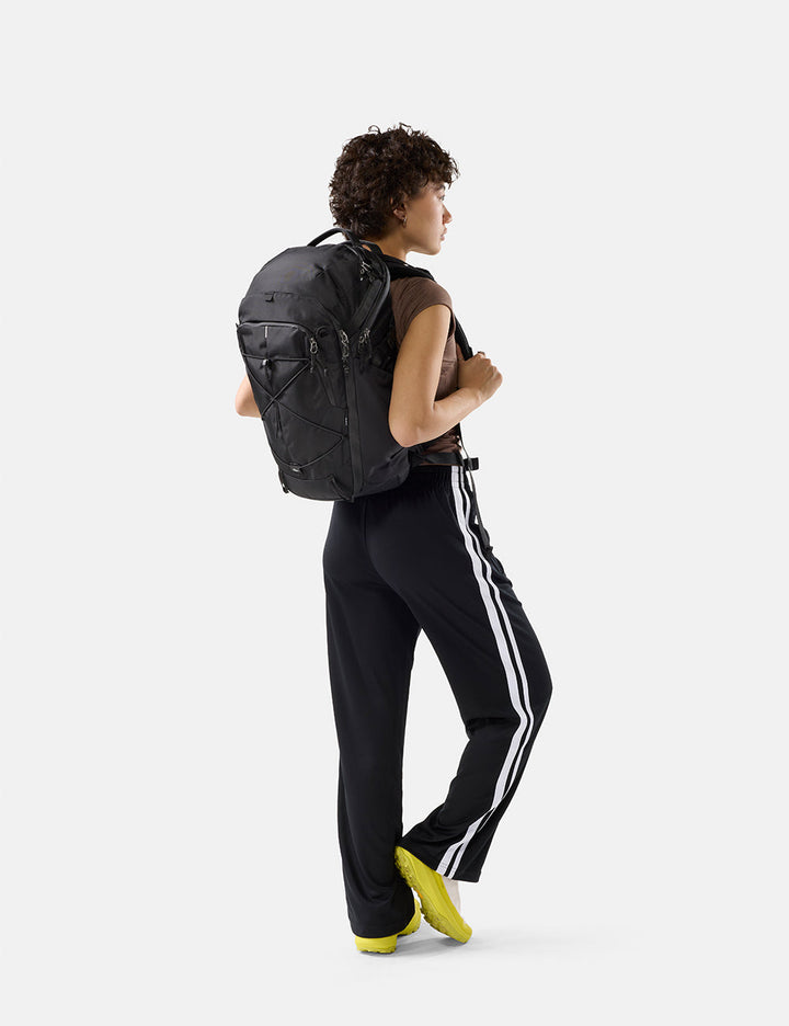 Matador 24L Adventure Pack in Black - person wearing a black backpack and black pants with white stripes on a white background