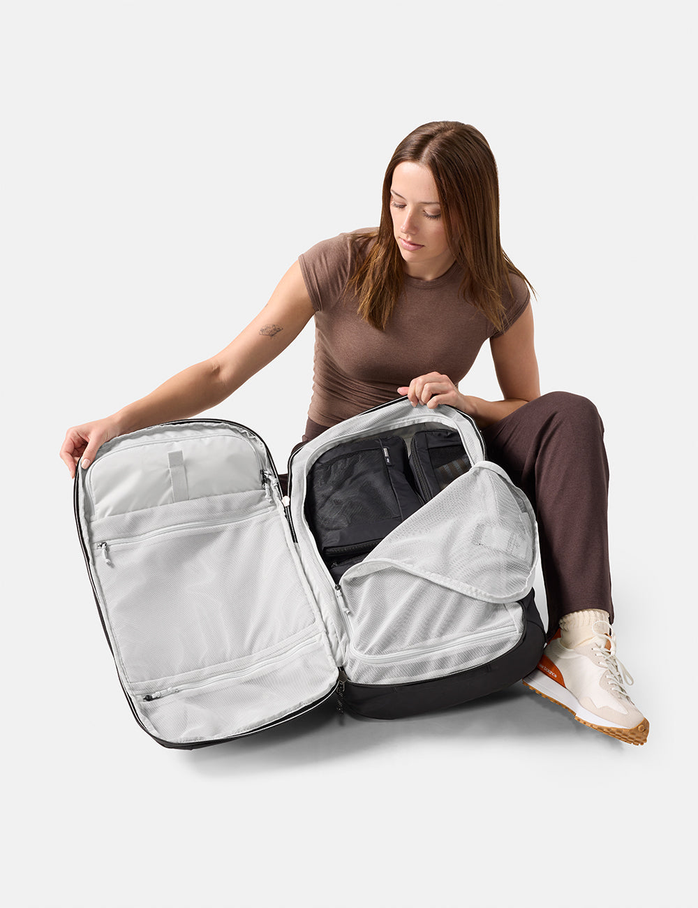 Matador 45L Global Travel Pack in Black - woman sitting on the floor with a large open backpack, showing its compartments