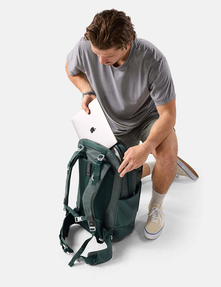 Matador 45L Global Travel Pack in Juniper - man placing a laptop into a green backpack on a white background