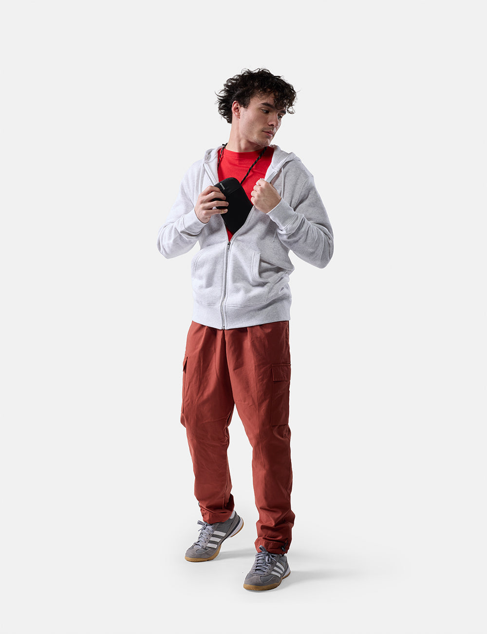 Matador Global Travel Stash in Black - man on white background placing travel neck wallet inside his zip up sweatshirt