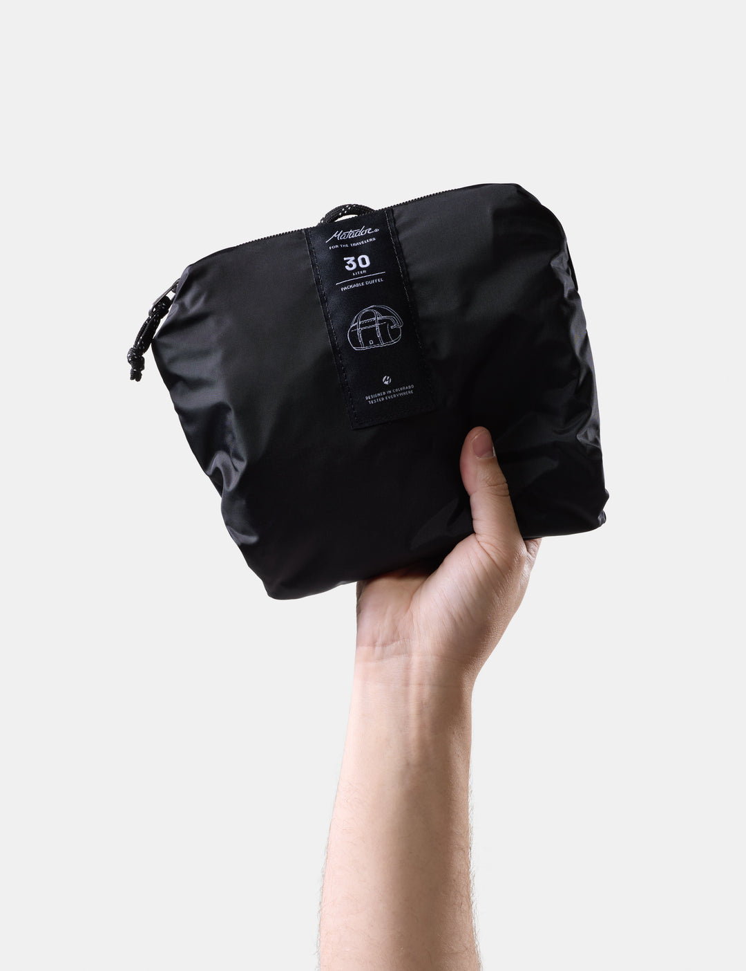 Matador 30L Packable Duffel in Black - black compression bag held by a hand on a light gray background