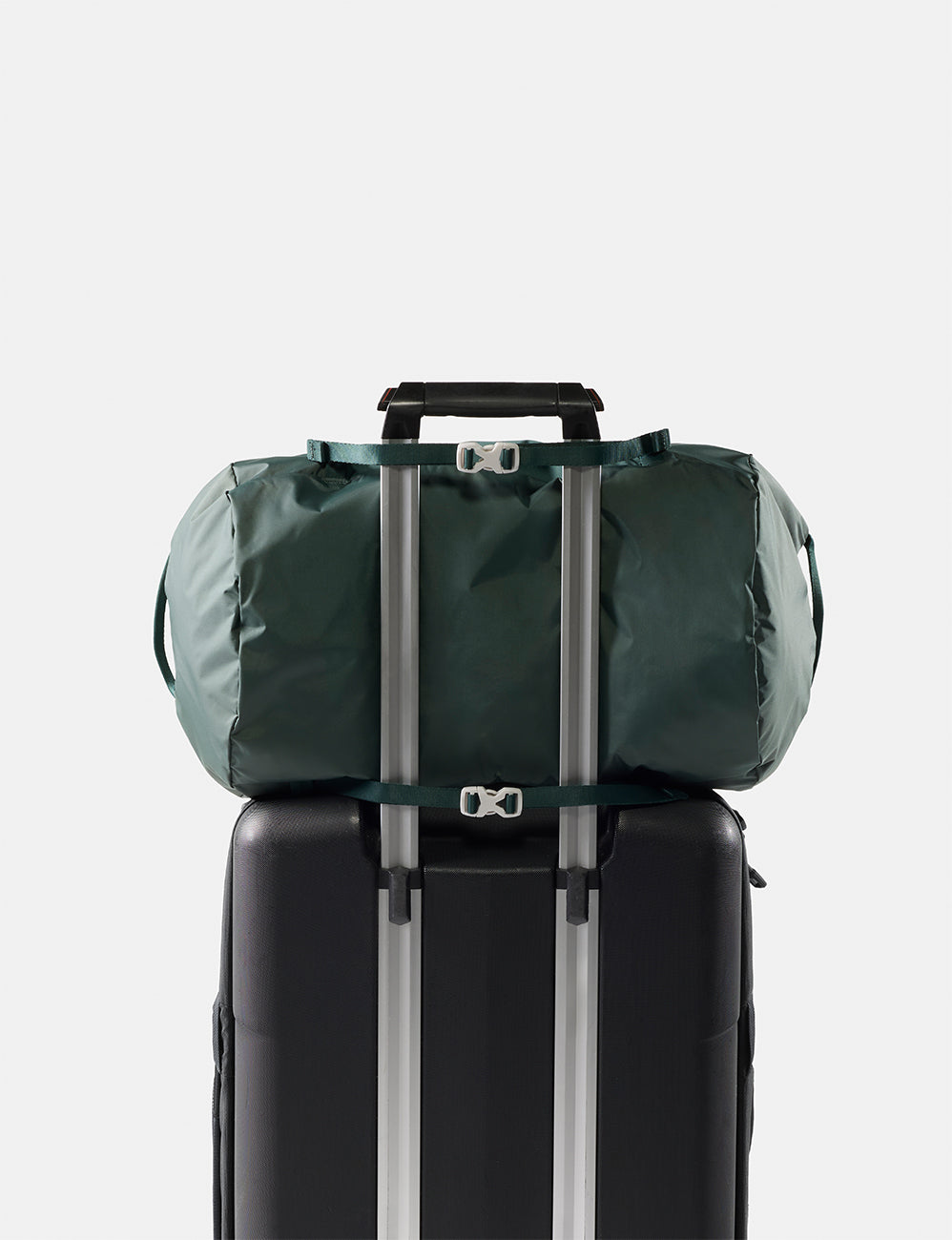 Matador 30L Packable Duffel in Juniper - green duffel bag tied to a black suitcase on a light gray background
