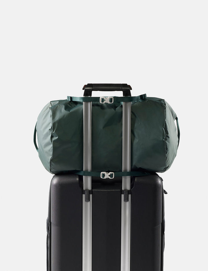 Matador 30L Packable Duffel in Juniper - green duffel bag tied to a black suitcase on a light gray background