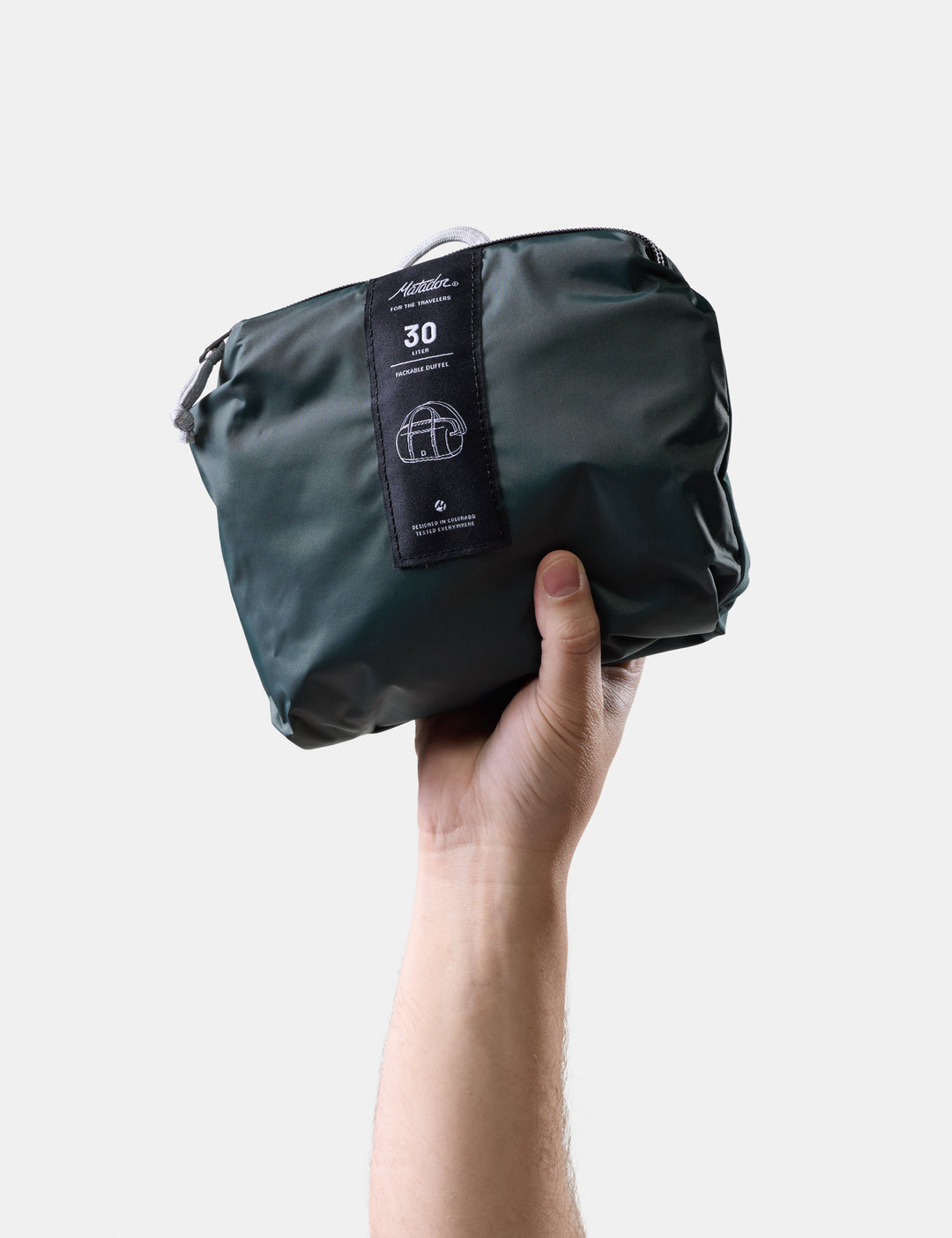 Matador 30L Packable Duffel in Juniper - hand holding a juniper compression bag with a visible brand label on a light gray background