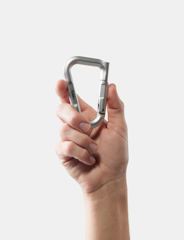 Matador BetaLock in Shadow Green - hand holding a metallic carabiner against a white background