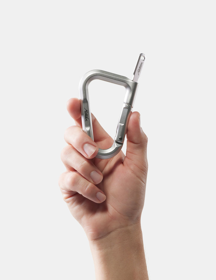 Matador BetaLock in Gold - hand holding a silver carabiner against a white background