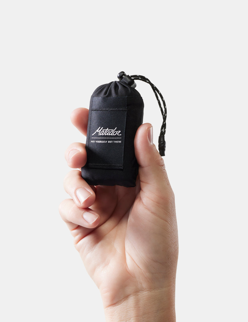 Matador Mini Pocket Blanket™ 4.0 - 110 x 70cm in Black - hand holding a black drawstring pouch with a brand logo on a light gray background
