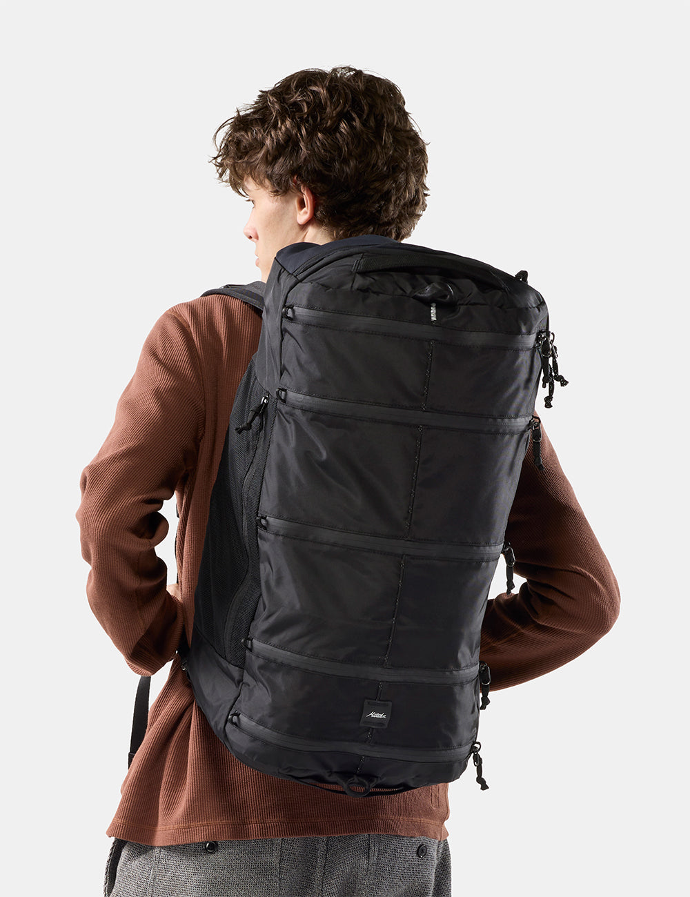 Matador 45L SEG Hybrid Travel Pack in Black - a man wearing a large black backpack, photographed from behind against a light gray studio background