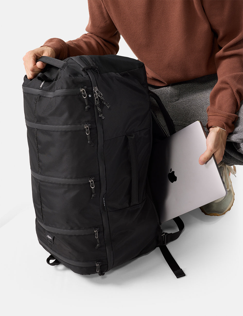 Matador 45L SEG Hybrid Travel Pack in Black - person holding a black backpack and a laptop on a white background