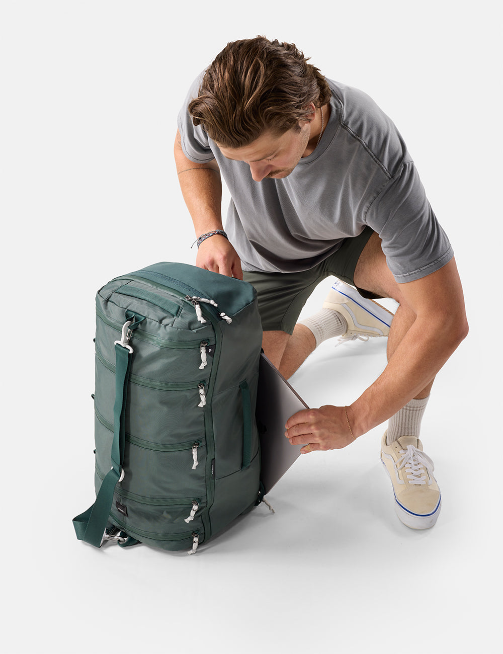 Matador 45L SEG Hybrid Travel Pack in Juniper - man unpacking a green backpack on a white background
