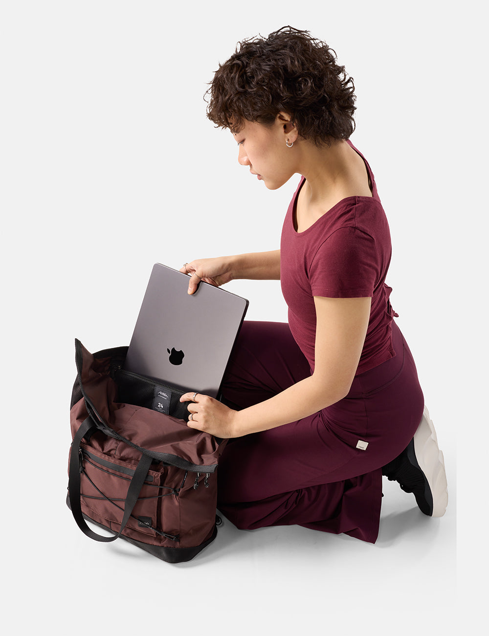 Matador 24L Tote Pack in Garnet - woman in a burgundy dress placing a laptop into a garnet backpack on a white background